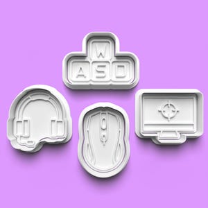 Może przedstawiać: Zestaw pięciu białych plastikowych foremek do ciasteczek w kształcie akcesoriów do gier: słuchawek, myszki, klawiatury z literami "WASD" i monitora komputerowego z tarczą w środku.