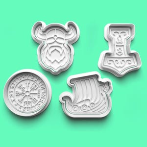 May include: Set of four white plastic cookie cutters featuring Viking-themed designs: a Viking with a beard, a ship, a compass, and a hammer.
