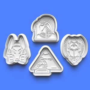 May include: Set of four white plastic cookie cutters shaped like Egyptian symbols: a pyramid, a scarab beetle, a pharaoh, and an anubis jackal.
