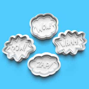 May include: Four white plastic cookie cutters shaped like speech bubbles with the words "POW!" "WHAM!" "WOW!" and "ZAP!" in a comic book style font.