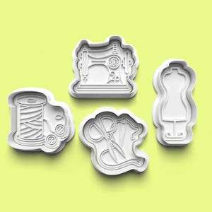May include: Four white plastic cookie cutters in the shapes of sewing-related items. The shapes include a spool of thread, a sewing machine, scissors with thread, and a dress form. The background is a light green colour.