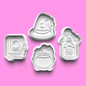 May include: Four white plastic cookie cutters with a Halloween theme. The shapes include a witch's hat with a crescent moon, a cauldron with stars, a potion bottle with a skull and crossbones, and a spell book with a crystal ball.