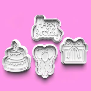 Peut inclure: Ensemble de quatre emporte-pièces en plastique blanc, représentant un gâteau d'anniversaire, des ballons, un coffret cadeau et les mots "Joyeux anniversaire".