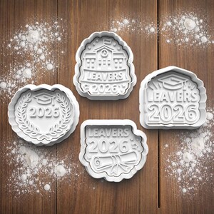 May include: Four white cookie cutters with graduation-themed designs. One cutter features a graduation cap within a laurel wreath and the year 2026. Other cutters display the text "LEAVERS 2026" with a school building, a graduation cap, and a diploma.