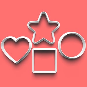 Può includere: Quattro formine bianche per biscotti a forma di cuore, stella, quadrato e cerchio. Sono disposte su uno sfondo rosso. Le formine sono realizzate in un materiale bianco spesso.