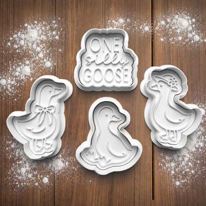 Peut inclure: Quatre emporte-pièces en plastique blanc en forme d'oies et l'expression "ONE silly GOOSE". Une oie a un nœud, une autre un chapeau. Les emporte-pièces sont sur une surface en bois avec de la farine.