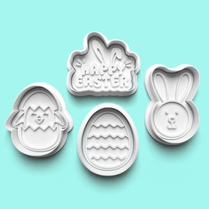 Puede incluir: Cuatro cortadores de galletas blancos con temática de Pascua sobre un fondo azul claro. Las formas incluyen un pollito saliendo de un huevo, un huevo de Pascua con un patrón en zigzag, una cara de conejito y un cortador en forma de nube con las palabras "Happy Easter".