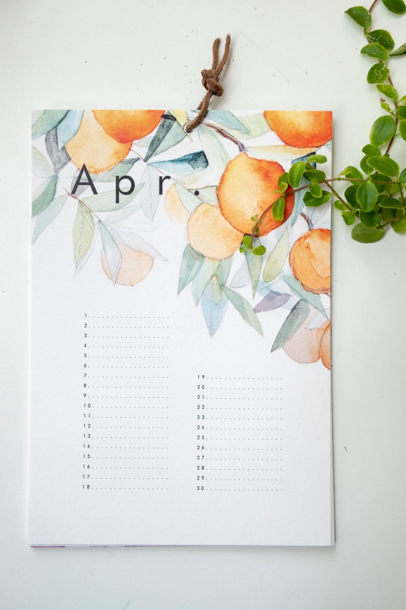 May include: A watercolour calendar featuring a branch of orange trees with leaves and fruit. The calendar is for the month of April and has a brown leather hanging loop.