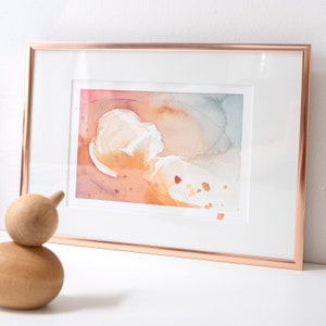 May include: A framed watercolour painting with abstract shapes in shades of orange, pink, and blue. The painting is set against a white background.