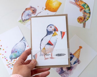 May include: A set of five greeting cards featuring watercolour illustrations of animals. The cards are blank inside and perfect for sending a special message. The cards feature a puffin with party flags, a squirrel with a balloon, a chameleon, a pigeon, and a badger.