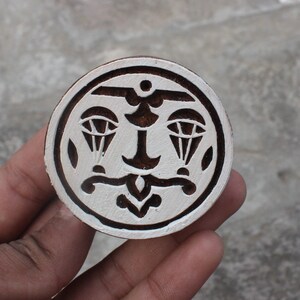 May include: A round wooden block printing stamp with a white background and a black design of two parachutes with an anchor in the middle.