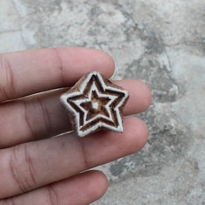 May include: A wooden block carving of a star with a white outline. The star has a smaller star inside of it.