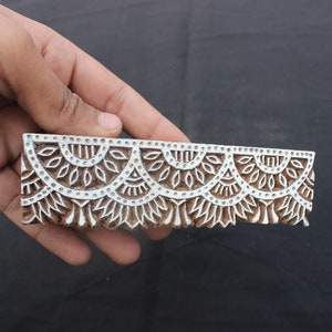 May include: A wooden printing block featuring a repeating pattern of half-circles and floral designs. The block is intricately carved and is ready for use in textile printing.