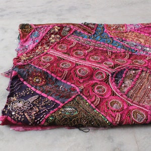May include: A pink, purple and gold patchwork throw pillow with intricate embroidery and beaded details.