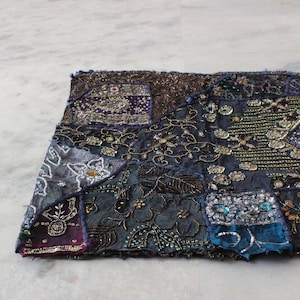Könnte beinhalten: Ein Patchwork-Teppich in Blau-, Lila- und Brauntönen. Der Teppich ist mit Pailletten und Perlen verziert, was ihm einen schimmernden Effekt verleiht.