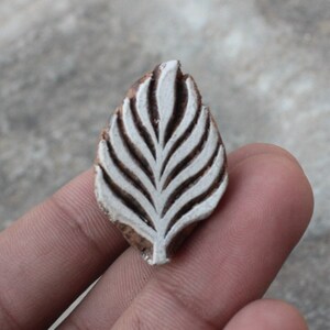 May include: A wooden block printing stamp with a white leaf design. The stamp is carved with intricate details and is ready to be used for creating patterns on fabric or paper.