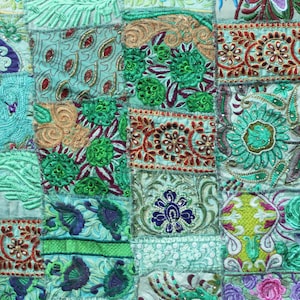Op de afbeelding: Een patchworkdeken met een teal achtergrond en kleurrijke geborduurde ontwerpen. De deken is gemaakt van veel verschillende vierkanten, elk met een uniek patroon. De deken is een prachtig voorbeeld van traditioneel Indiaas handwerk.