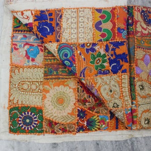 May include: A colourful patchwork throw pillow featuring a variety of floral and geometric patterns in shades of orange, blue, green, and white. The pillow is made from fabric scraps sewn together to create a unique and textured design.