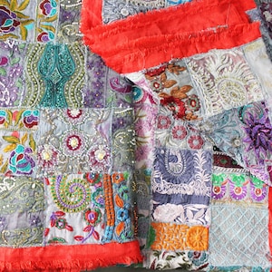 Puede incluir: Una colcha de retazos con una variedad de diseños bordados coloridos y lentejuelas. La colcha está hecha de diferentes telas y texturas, y tiene un borde de flecos rojos.