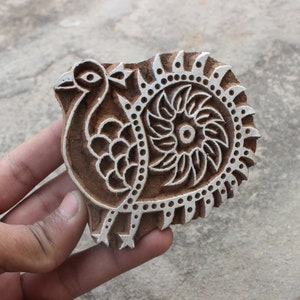 Puede incluir: Un bloque de impresión de madera con un diseño detallado de un pavo real y un motivo floral. El bloque está tallado con detalles intrincados y está listo para ser utilizado para la impresión textil.