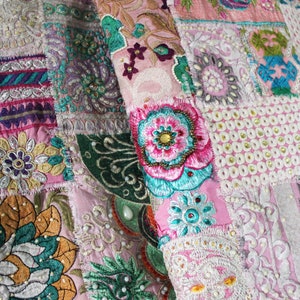 May include: A pink fabric patchwork with colorful embroidered flowers and intricate patterns. The fabric is made of different textures and materials, creating a unique and visually appealing design.