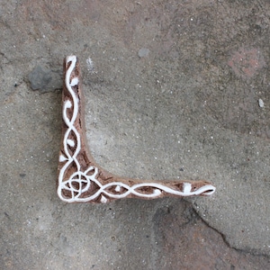 May include: A brown wooden block with a white design carved into it. The design is a corner pattern with a floral motif.