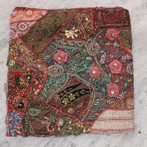 Op de afbeelding: Een kleurrijk patchwork kussenovertrek met ingewikkelde borduursels en pareldetails. De hoes is gemaakt van verschillende stoffen in tinten rood, bruin, groen en goud, met een bloemenmotief over de hele hoes.