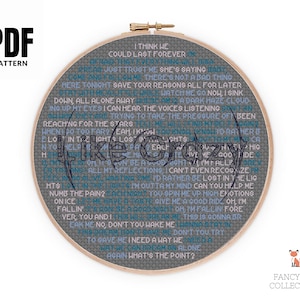 May include: A round embroidery hoop with the words "Like Crazy" and song lyrics in a gray and blue color scheme. The text is stitched on a gray fabric. The words "PDF PATTERN" are in the upper left corner.