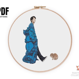 Op de afbeelding: Een kruissteekpatroon in een houten borduurring. Het ontwerp toont een persoon in een blauwe pufferjas, lopend naast een bruin konijn. De tekst "PDF PATTERN" staat linksboven.