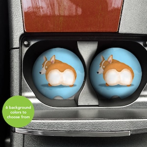 May include: Two blue and white car cup holders with a cartoon image of a corgi dog with a brown and white coat. The corgi is facing away from the viewer and has its tail curled up.