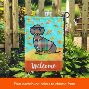 May include: A garden flag featuring a cartoon dachshund wearing a plaid shirt and bow tie. The flag has a blue background with falling leaves and the word "Welcome" at the bottom.