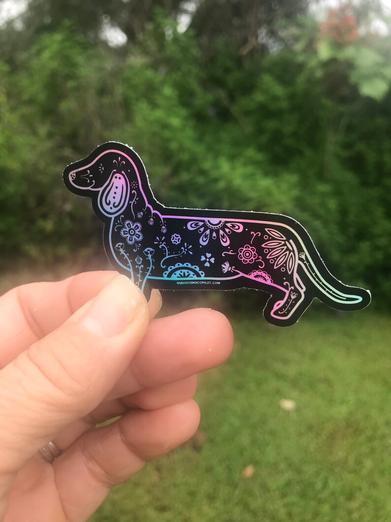 May include: A black and white dachshund silhouette sticker with a floral design. The sticker has a holographic finish that shifts between pink and blue.