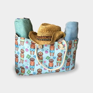 May include: A blue and white tote bag with a pattern of dogs wearing sunglasses and swimsuits. The bag has a straw hat and two towels inside.