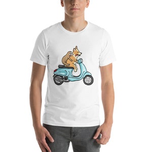 May include: A white t-shirt with a cartoon image of a corgi and a sloth riding a blue scooter.