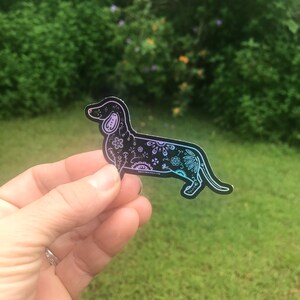 May include: A black and white dachshund sticker with a floral design. The sticker has a holographic finish that shifts from pink to blue.