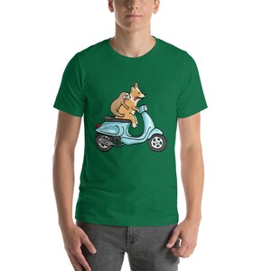 May include: A green t-shirt featuring a cartoon illustration of a corgi and a sloth riding a blue scooter.