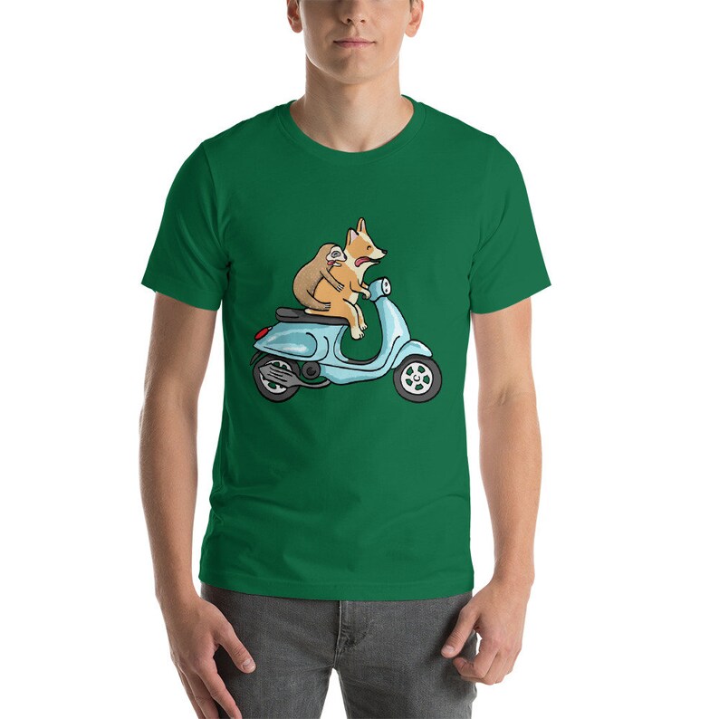 May include: A green t-shirt featuring a cartoon illustration of a corgi and a sloth riding a blue scooter.
