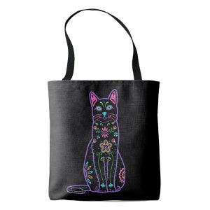 Puede incluir: Una bolsa de tela negra con un dise&ntilde;o de gato colorido del D&iacute;a de Muertos. El gato est&aacute; delineado en morado y tiene orejas rosas, ojos azules y una variedad de flores y dise&ntilde;os coloridos en su cuerpo.