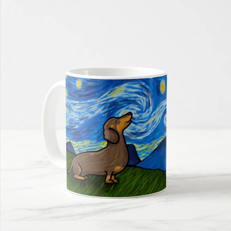 Op de afbeelding: Een witte keramische koffiemok met een bruin dackelhond silhouet tegen een blauwe en gele sterrenhemel. De hond kijkt omhoog naar de hemel en de achtergrond doet denken aan Vincent van Gogh's Sterrennacht.