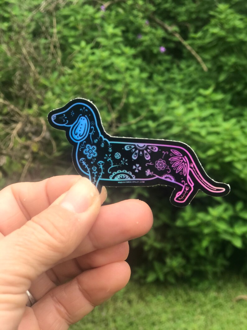 May include: A black vinyl sticker of a dachshund with a colorful floral pattern. The sticker has a gradient of blue and pink colors.