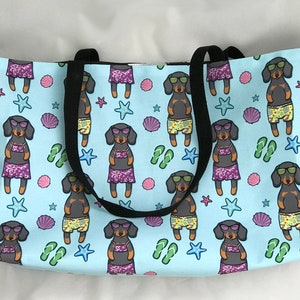 May include: A light blue tote bag featuring a repeating pattern of black and brown dachshunds wearing sunglasses and swimwear. The dachshunds are surrounded by seashells, starfish, and flip-flops.