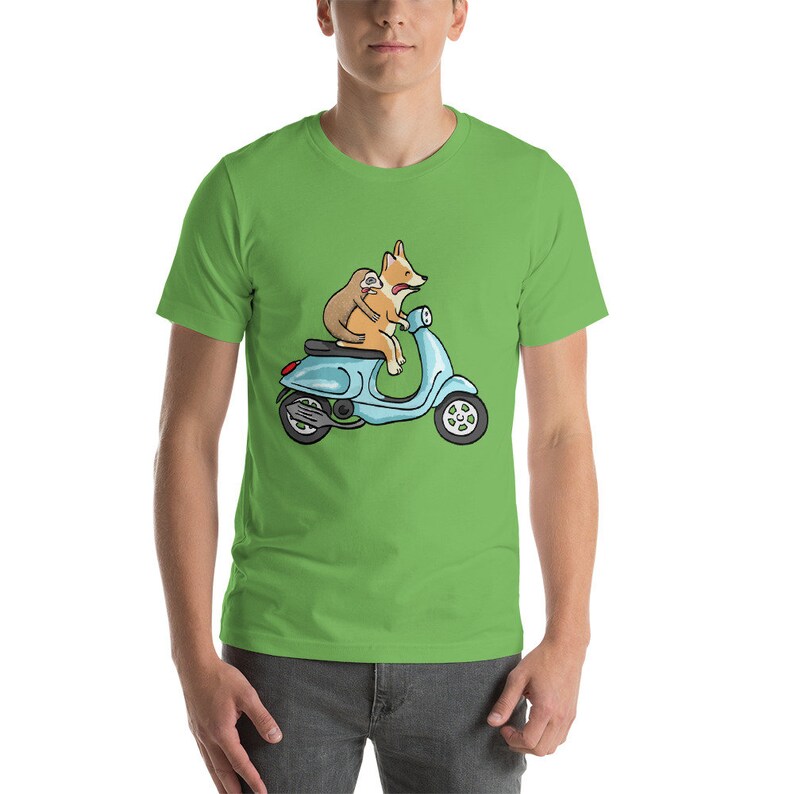 May include: A green t-shirt with a cartoon image of a corgi driving a blue scooter with a sloth riding on its back.