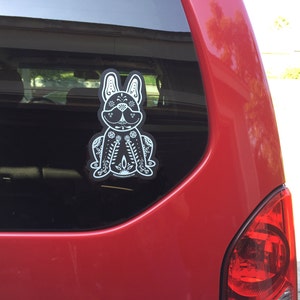 May include: A black and white sticker of a French bulldog with a floral design on a red car.