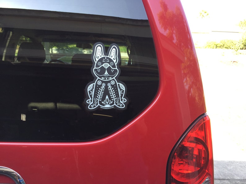 May include: A black and white sticker of a French bulldog with a floral design on a red car.