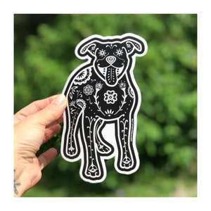 May include: Black and white sticker of a dog with a floral design. The dog is standing on all four legs and has its tongue sticking out. The sticker is cut out in the shape of the dog.