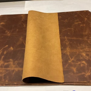 May include: A stack of brown leather sheets with a folded sheet of tan leather on top. The leather has a distressed, vintage look.