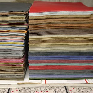 May include: Stacks of colorful felt sheets in various shades, including red, brown, blue, and green. The felt is neatly arranged in rectangular piles, showcasing a diverse palette of colors. The image highlights the texture and variety of the felt.