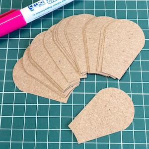 May include: A collection of die-cut, petal-shaped pieces of brown cardstock. The pieces are arranged on a green grid cutting mat, with a pink marker in the upper left corner. The cardstock has a textured, speckled appearance.