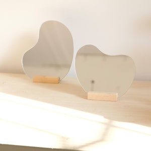 Peut inclure: Deux miroirs de forme libre avec un support en bois. Les miroirs sont en verre et ont une surface réfléchissante. Les supports sont en bois et sont de couleur brun clair.
