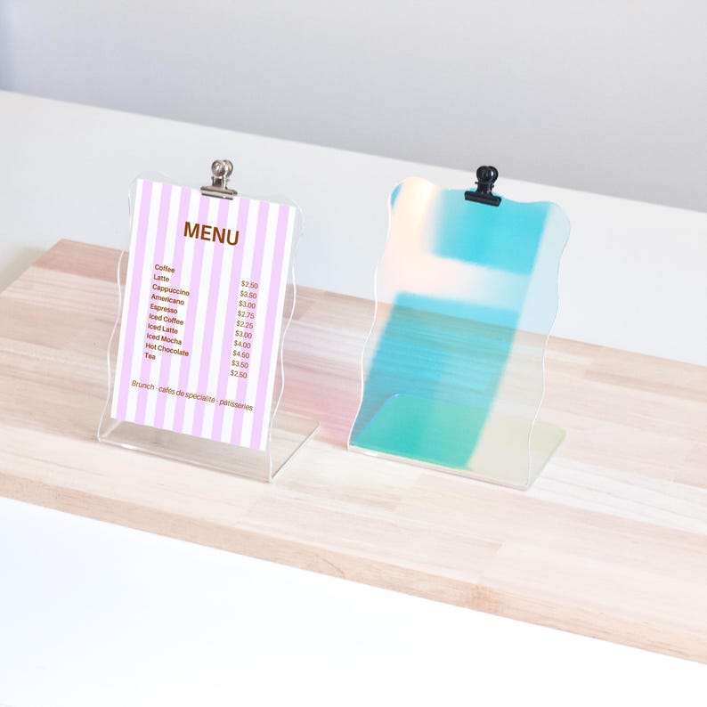 May include: Two clear acrylic sign holders with wavy edges. The left holder has a pink and white striped paper with a menu listing coffee and tea prices. The right holder is iridescent blue and green.